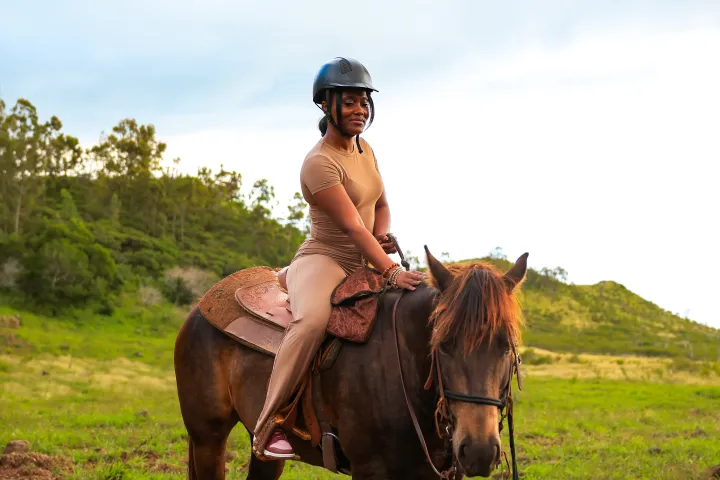 Person in helmet riding a brown horse on grassy terrain.