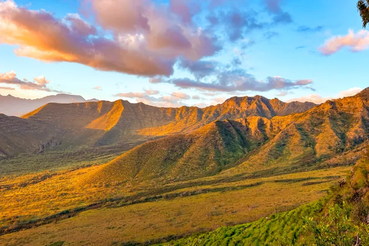 Sunlit mountains with scattered clouds in a blue sky.