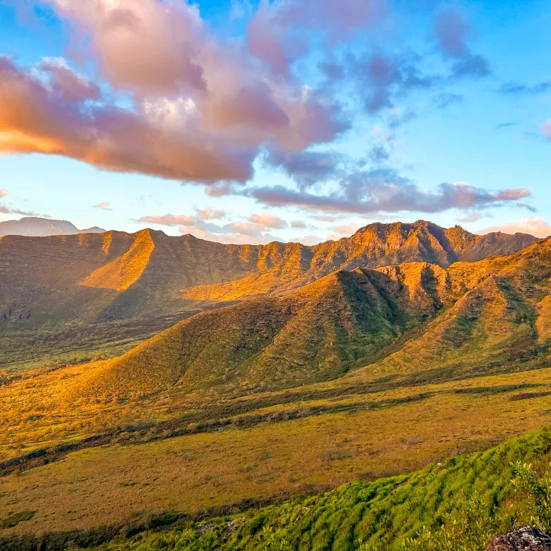 Sunlit mountains with scattered clouds in a blue sky.