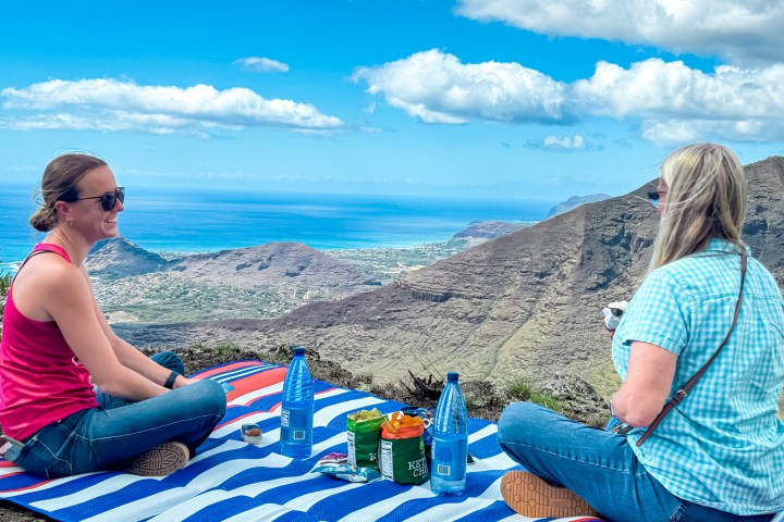 Two people having a picnic on a mountain with an ocean view.