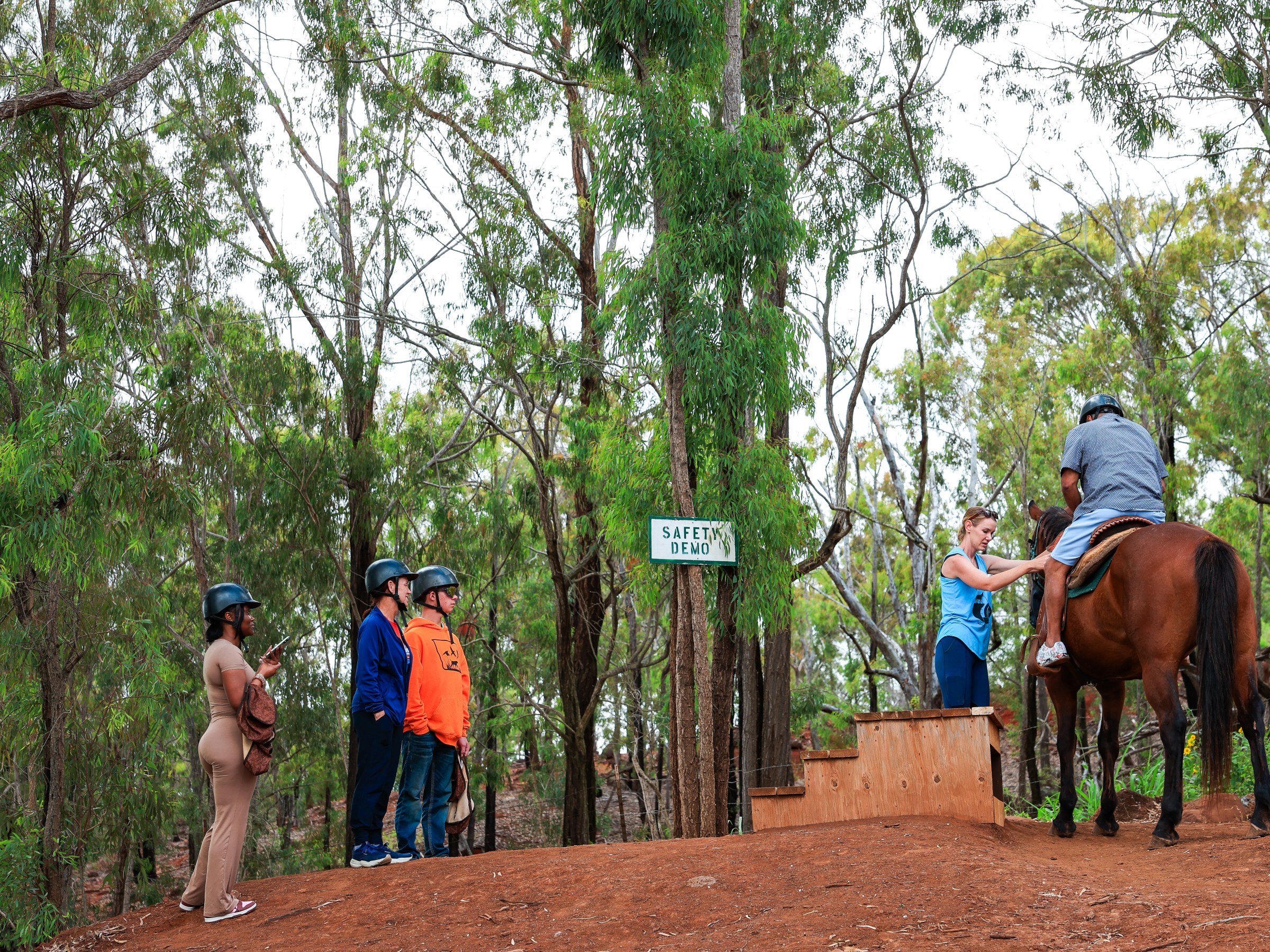People on horseback while others watch in a wooded area under a 'Safety Bump' sign.